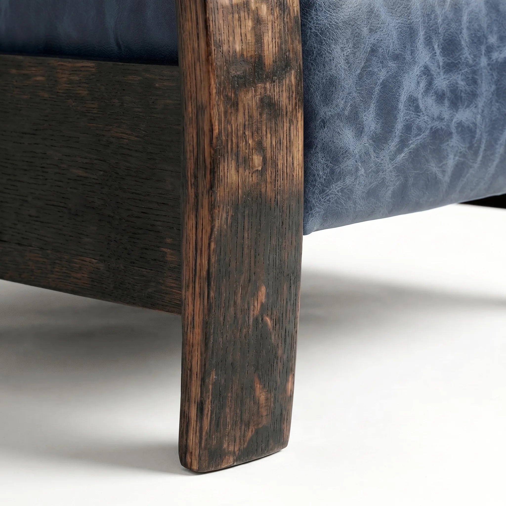Close-up of the Big & Tall whiskey barrel recliner's oak whiskey-barrel stave leg in denim blue leather, on a white background